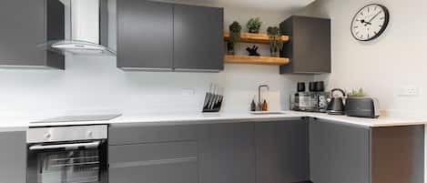 A modern kitchen with grey cabinets, a built-in oven, a coffee machine, and a clock on the wall.