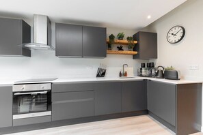 A modern kitchen with grey cabinets, a built-in oven, a coffee machine, and a clock on the wall.