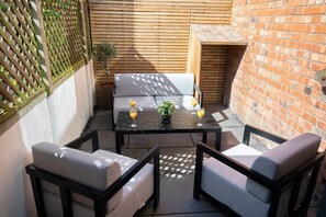 A patio with a table and two chairs, a potted plant, and a brick wall.