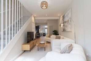 A modern living room with a staircase, a dining area, and a kitchen in the background.