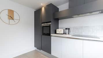 A modern kitchen with grey cabinetry, a built-in oven, a coffee maker, and a wall clock.
