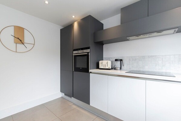 A modern kitchen with grey cabinetry, a built-in oven, a coffee maker, and a wall clock.