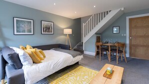 A bedroom with a bed, bedside table, lamp, and a dining area with a table and chairs. - Peaceful & Spacious 2 Bed Home in Cheltenham (Gloucestershire)