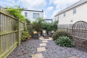 A garden with a wooden fence, a stone pathway, and outdoor furniture. - Peaceful & Spacious 2 Bed Home in Cheltenham (Gloucestershire)