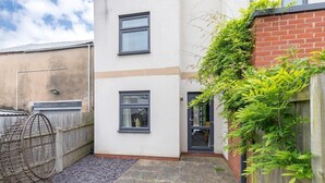 A small, enclosed courtyard with a white building, two windows, a door, and a wooden fence. - Peaceful & Spacious 2 Bed Home in Cheltenham (Gloucestershire)