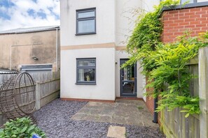 A small, enclosed courtyard with a white building, two windows, a door, and a wooden fence.