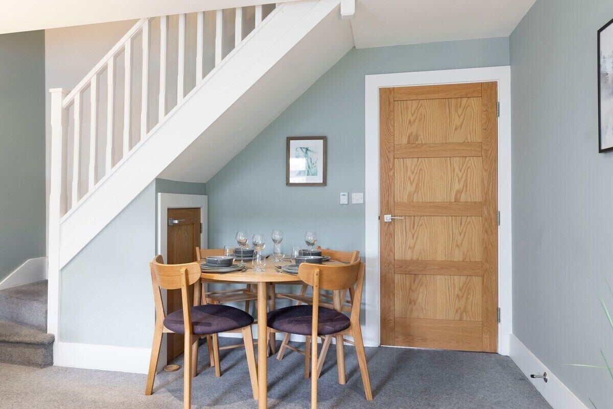 A dining area with a wooden table and chairs, a staircase, and a wooden door.