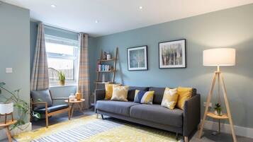A living room with a grey sofa, yellow cushions, a standing lamp, and a bookshelf.