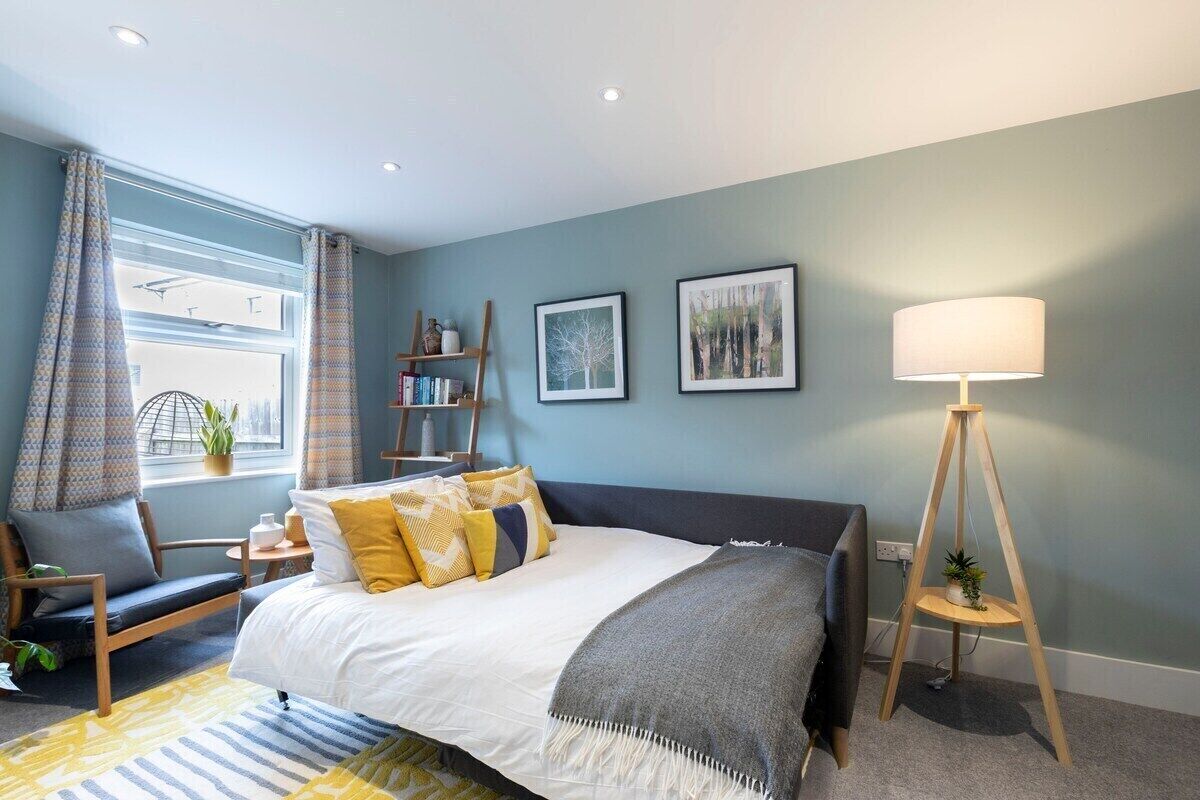 A modern bedroom with a bed, bedside table, lamp, and a view of the city through the window.