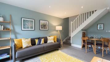 A living room with a grey sofa, yellow cushions, a wooden coffee table, and a staircase leading to a dining area.