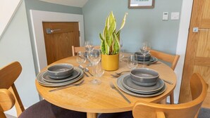 A dining table set with plates, bowls, cutlery, and glasses, surrounded by wooden chairs. - Peaceful & Spacious 2 Bed Home in Cheltenham (Gloucestershire)