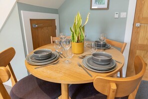 A dining table set with plates, bowls, cutlery, and glasses, surrounded by wooden chairs.