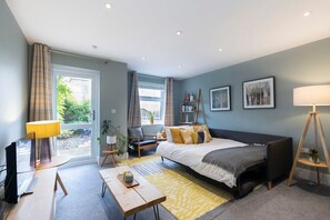 Une chambre moderne avec un lit, une table de chevet, une lampe et une vue sur la verdure à l’extérieur.