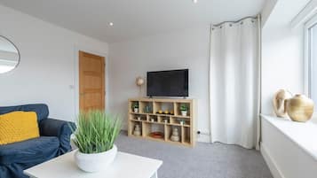 Una sala moderna con un sofá, una mesa de centro, un televisor sobre un mueble de madera y una ventana con cortinas.