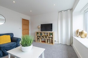 Un salon moderne avec un canapé, une table basse, un téléviseur posé sur un meuble en bois et une fenêtre avec des rideaux.