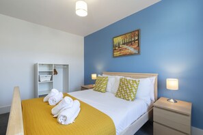 A hotel room with a bed, a nightstand, a bedside table, a wardrobe, and a painting on the wall.