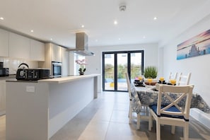 Una cocina moderna con armarios blancos, una isla central y un comedor con una mesa para cuatro.