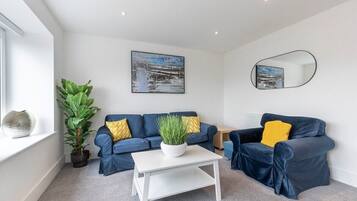A modern living room with two dark blue sofas, a white coffee table, a large potted plant, and a painting on the wall.