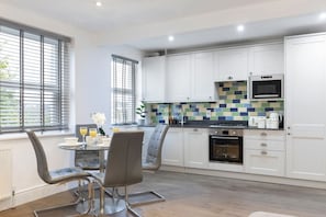 A modern kitchen with white cabinets, a tiled backsplash, and a dining area with two chairs and a table.