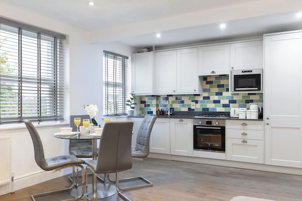 Una cocina moderna con armarios blancos, salpicadero de azulejos y una zona de comedor con dos sillas y una mesa.