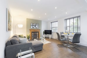 Una sala de estar moderna con sofá, televisor, chimenea, comedor y ventanas amplias.