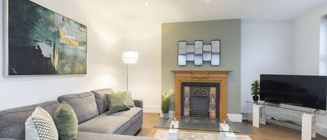 A modern living room with a grey sofa, a fireplace, a flat-screen TV, and a large abstract painting.