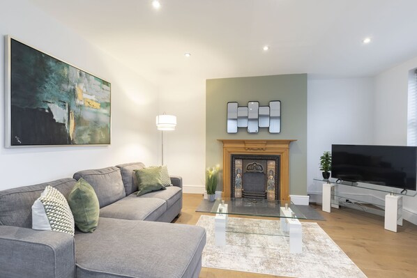 A modern living room with a grey sofa, a fireplace, a flat-screen TV, and a large abstract painting.