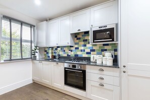 Una cocina moderna con armarios blancos, salpicadero azulejado, microondas, estufa y cafetera.