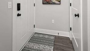 A hallway with white walls, a patterned rug, and a framed painting of a tree. - Bettendorf Gem: 2BR Condo w/ King Bed & Garage (Bettendorf)