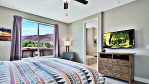 A hotel room with a large bed, a TV, a desk, and a view of the mountains.