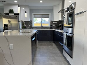 Une cuisine moderne dotée d’appareils électroménagers en acier inoxydable, d’un grand îlot central et offrant une vue sur l’extérieur.