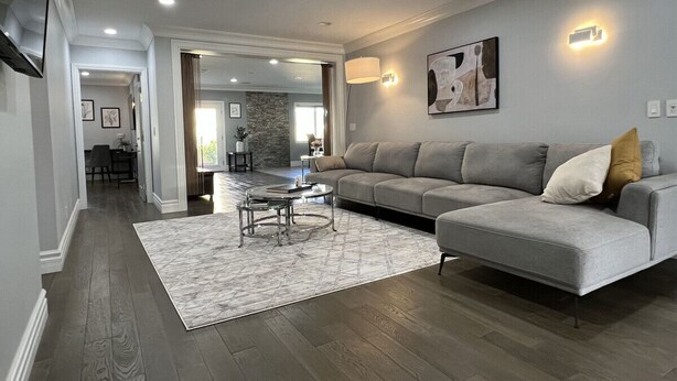 A modern living room with a grey sofa, a patterned rug, and a dining area in the background.