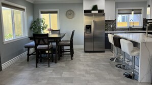 A modern kitchen with a dining area, a stainless steel refrigerator, and a bar with stools.