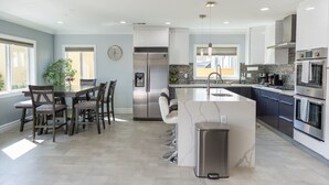 A modern kitchen with a central island, stainless steel appliances, and a dining area with chairs.