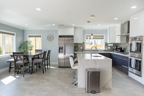 A modern kitchen with a central island, stainless steel appliances, and a dining area with chairs.