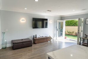 A modern living room with a flat-screen TV, a wooden cabinet, a large vase, and a sliding glass door leading to a garden.