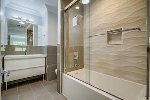 A modern bathroom with a glass-enclosed shower, a white vanity, and a textured wall.