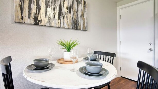 Een eettafel met vier kommen en wijnglazen, een potplant en een groot abstract schilderij aan de muur.