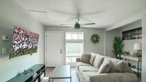 Een woonkamer met een bank, een salontafel, een televisie aan de muur en een plafondventilator.