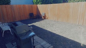 Een achtertuin met een barbecue, een metalen stoel en een houten omheining.