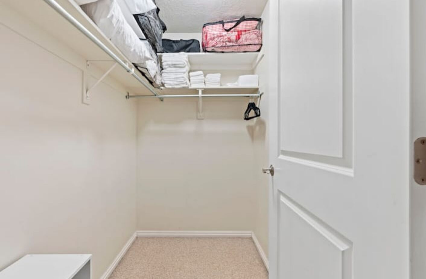 A small walk-in closet with a door, shelves, and hanging space.