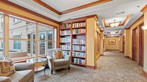 A library with bookshelves, a reading area with chairs, and a carpeted floor.