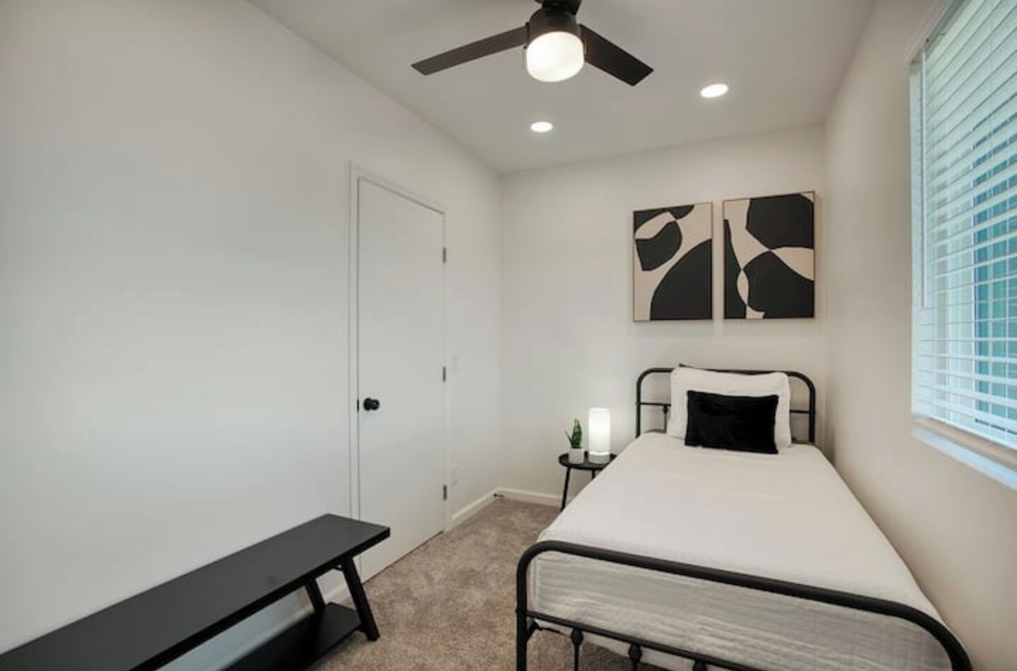 A bedroom with a bed, a bench, a ceiling fan, and abstract wall art.