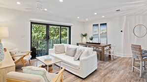Una sala de estar moderna con un sofá blanco, una mesa de centro de madera y un comedor con una mesa y sillas de madera.
