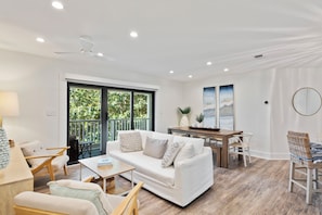 Una sala de estar moderna con un sofá blanco, una mesa de centro de madera y un comedor con una mesa y sillas de madera.