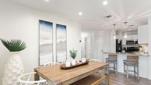 Una cocina moderna con armarios blancos, una mesa de comedor de madera y dos taburetes de mimbre.
