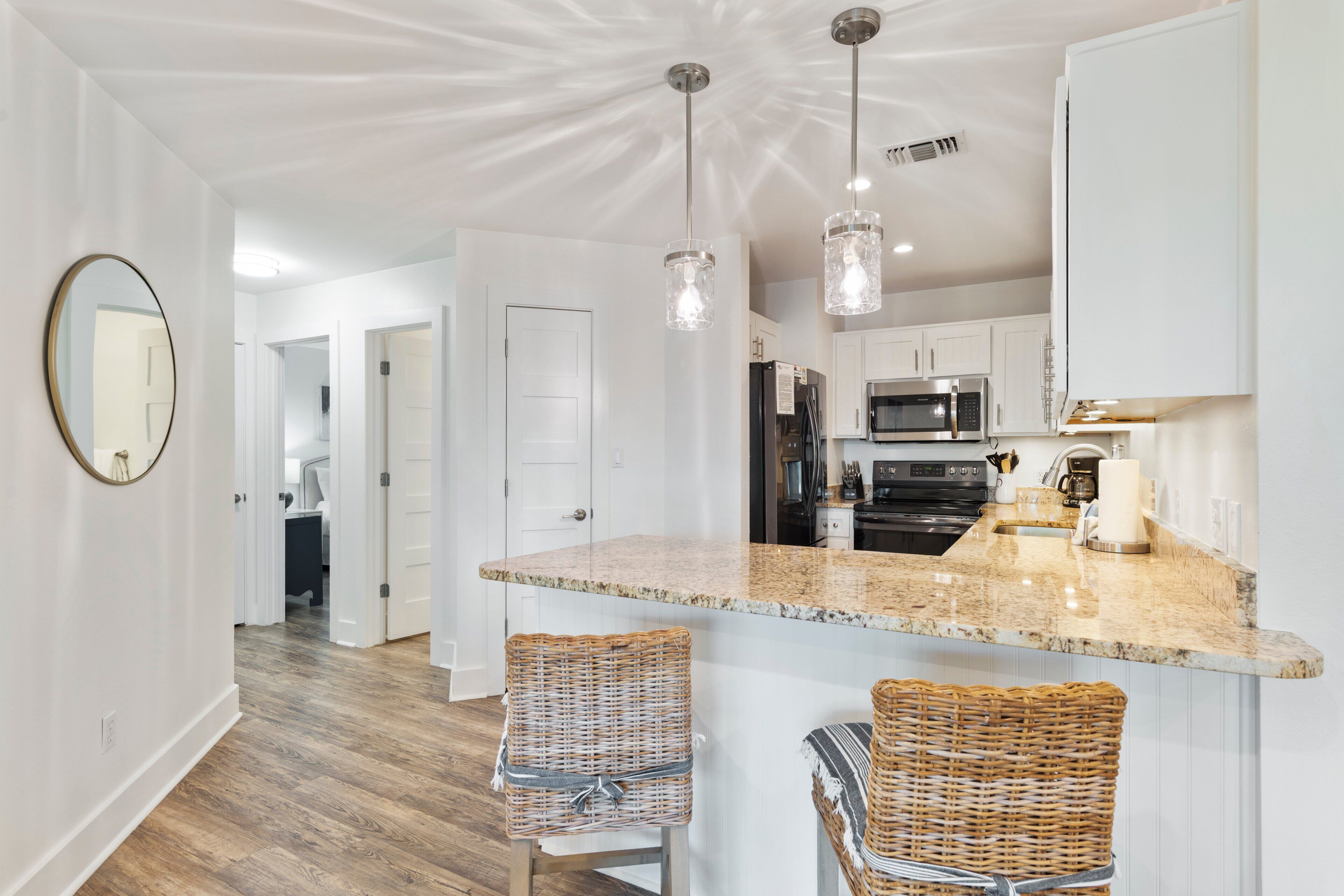 A kitchen with a granite countertop, stainless steel appliances, and wicker bar stools.