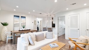 Una sala de estar moderna con un sofá blanco, una mesa de centro de madera y un comedor con una mesa y sillas de madera.