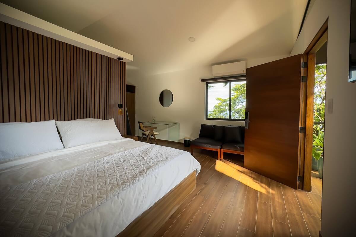 Quarto moderno com uma cama grande, uma escrivaninha e uma janela com vista para o verde.