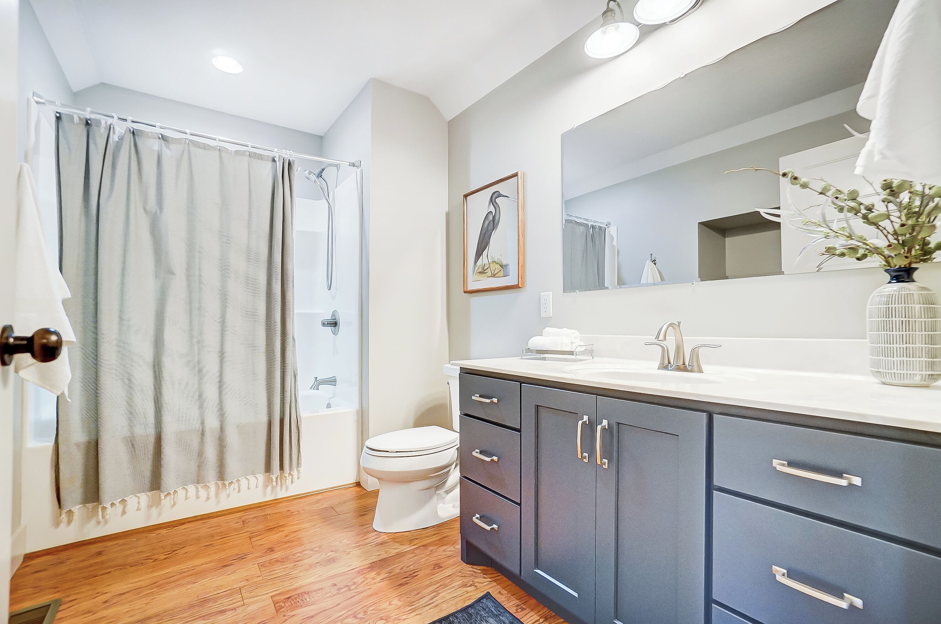 A modern bathroom with a shower curtain, toilet, vanity with drawers, and a large mirror.